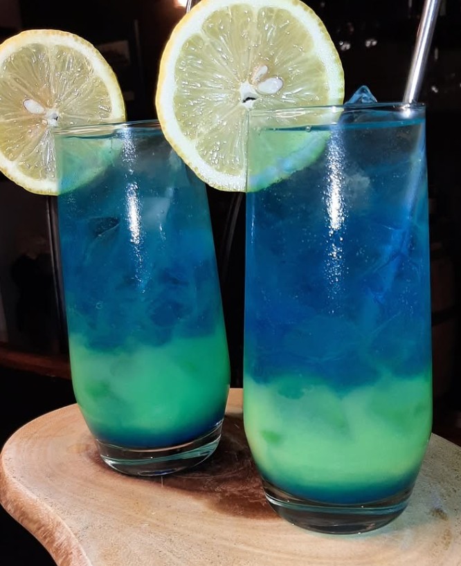 Bright arrangement of sparkler ingredients on a sunny counter: pulp-free orange juice carton, blue curacao bottle, champagne flute bottle chilling, Collins glass with ice, evoking fresh, vibrant citrus notes


