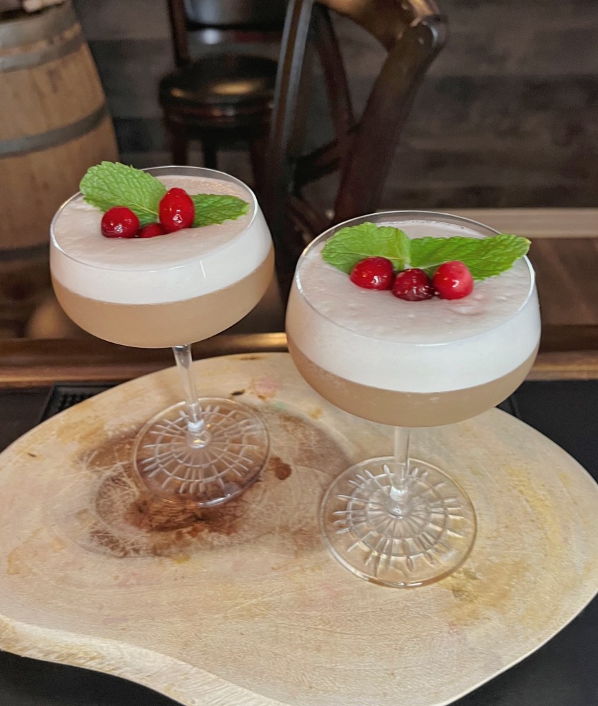 A homemade gin sour with lots of foam festively decorated with cranberries and mint leaves to look like holly.  
