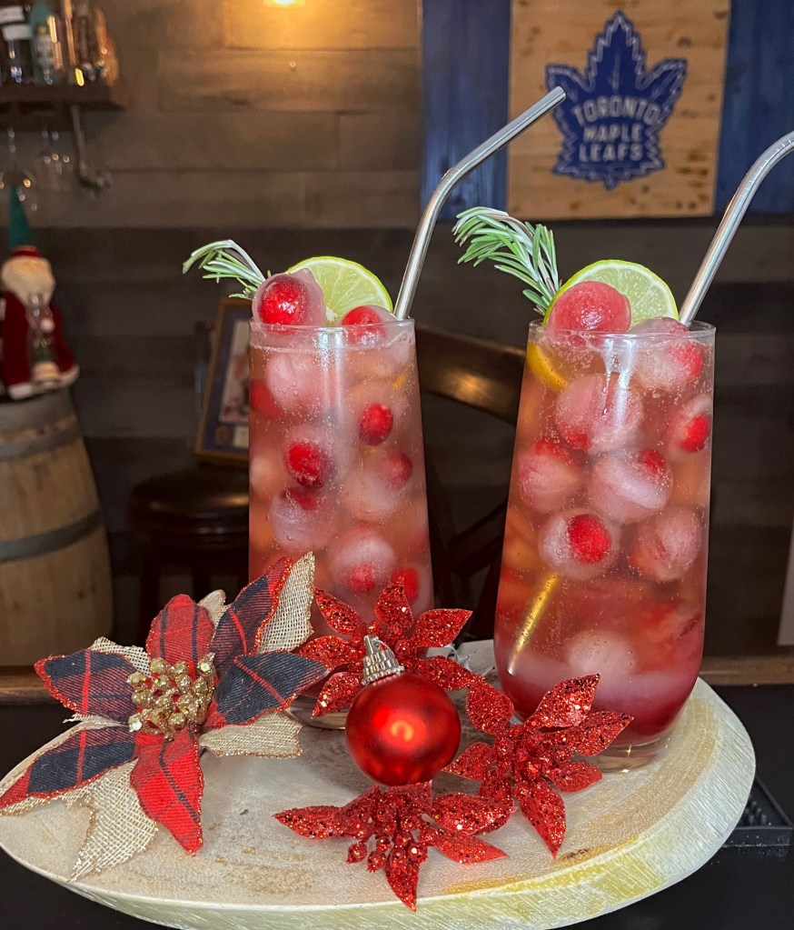A festive Christmas cocktail called "Rudolf's Polar Plunge" from Miller's Amish Pub, presented in a rocks glass filled with a deep red whiskey or bourbon drink (likely featuring cranberry). The humorous garnish depicts poor Rudolph the reindeer "frozen solid" in a polar plunge