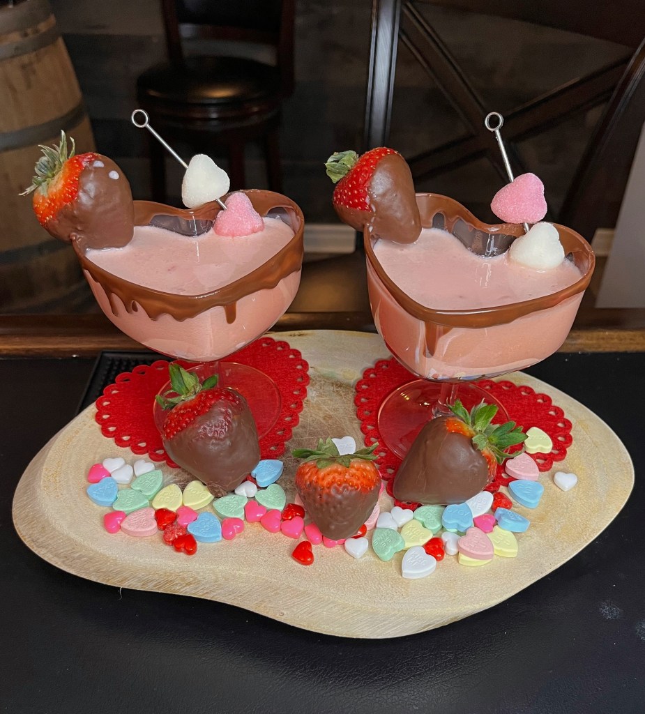Heart-shaped martini glass rimmed with chocolate, garnished with a chocolate-dipped strawberry, filled with a creamy pink strawberry-chocolate cocktail made with fresh muddled strawberries, Baileys, chocolate liqueur, vodka, and cream