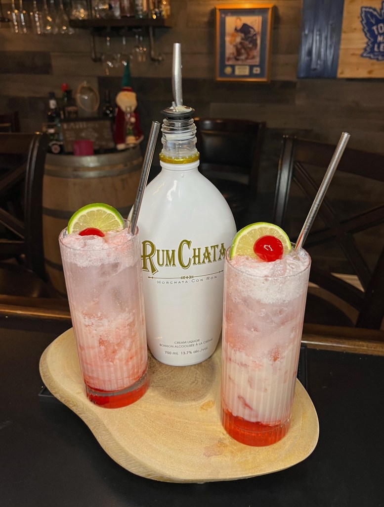 Two thin Collins Glasses contain a hand-crafted red and white cocktail that tastes like a tropical vacation!