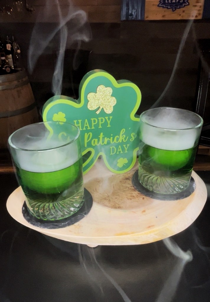 St. Patrick's Day Pot of Gold cocktail: a smoked Irish Whiskey Old Fashioned riff in a tumbler with a large ice ball, featuring Jameson Irish Whiskey, banana liqueur, maple syrup, pear bitters, and pecan wood smoke for a rich banana bread-inspired flavor.

