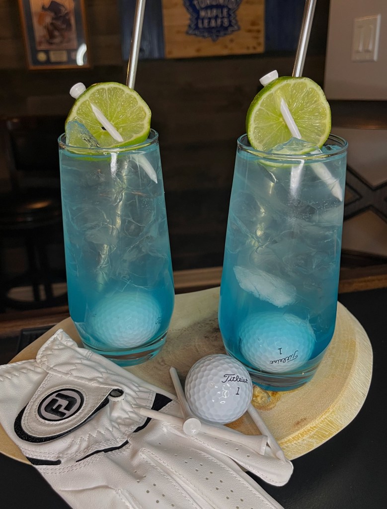 Bright blue Water Hazard cocktail in a tall 16oz Collins glass filled with ice, topped with fizzy Sprite, garnished with a fresh lime wheel, featuring vodka, blue Gatorade, fresh lime juice, and lemonade for a refreshing golf-inspired drink.

