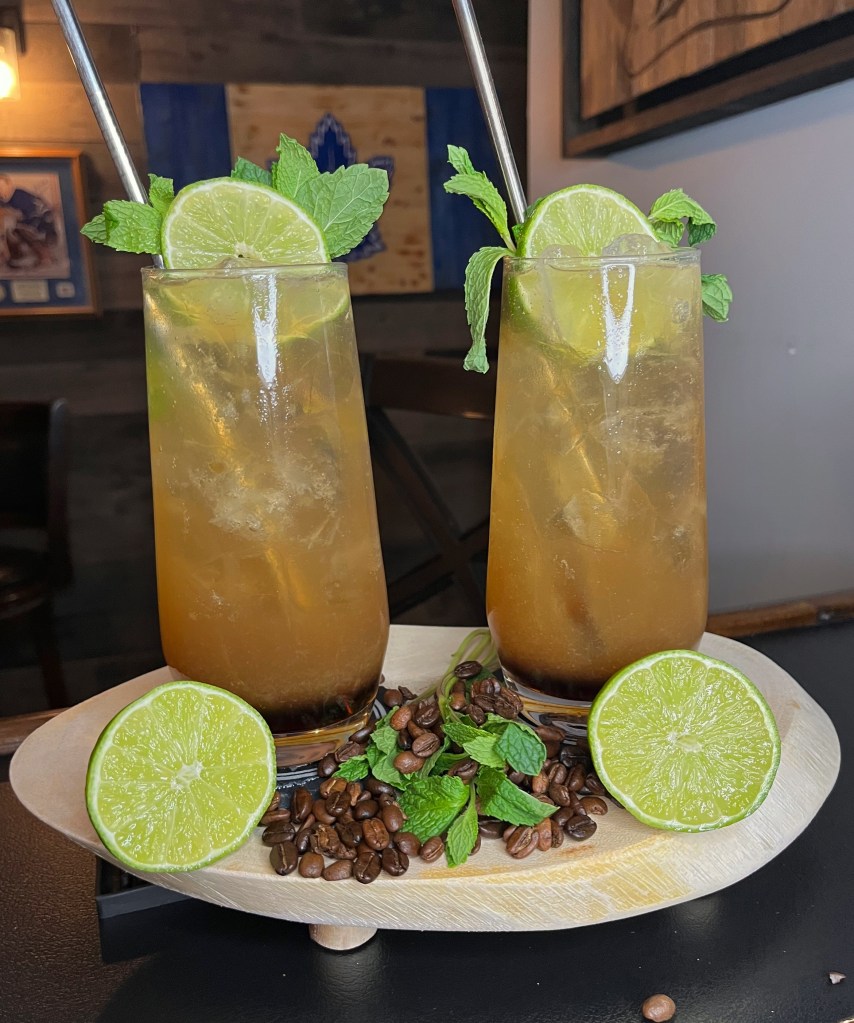 "Refreshing tequila cocktail in a tall 16oz Collins glass filled with ice, topped with ginger ale, featuring a vibrant lime wheel and fresh mint sprig garnish. Made with coffee liqueur, fresh lime juice, pineapple juice, and tequila for a tropical, zesty, and slightly caffeinated twist on a mule-style drink.

