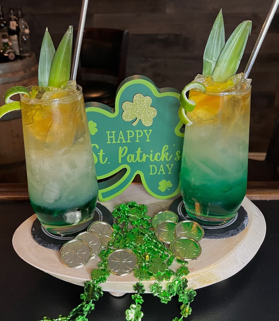 Vibrant tropical rum cocktail in a tall 16oz Collins glass: bright blue base from Blue Curacao layered with banana liqueur, topped with fizzy club soda, fresh pineapple juice, a dark rum float, and garnished with fresh pineapple fronds and a twisted lime peel. Sunny, refreshing vacation drink with a kick of Caribbean flavors

