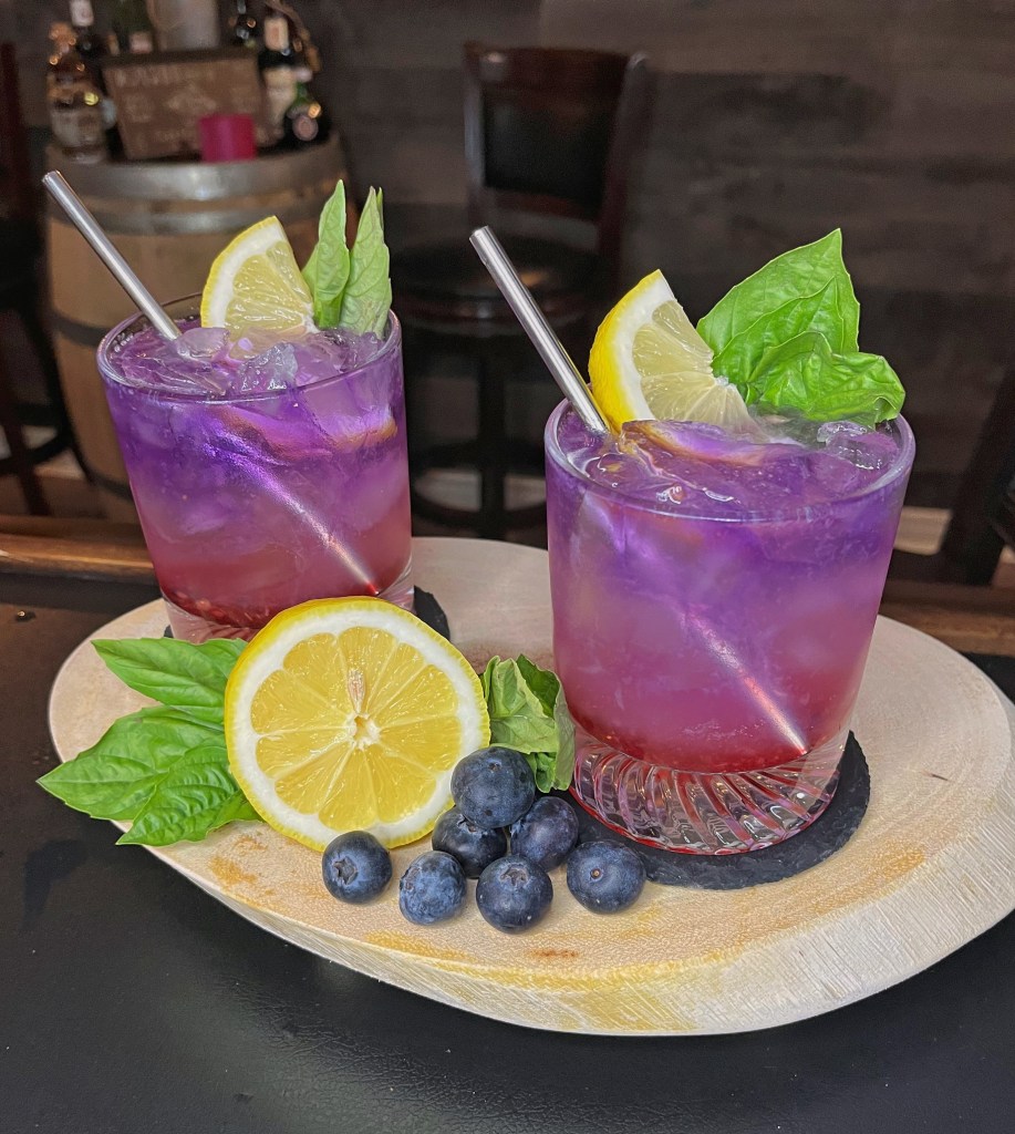 First basil cocktail in our series — a vibrant Blueberry Basil Gin Fizz in a 10oz tumbler. Muddled fresh blueberries and basil with blackberry syrup, fresh lemon juice, Empress Gin, and topped with club soda. Garnished with a lemon wheel and basil sprig. Stir before sipping for the perfect refreshing mix!

