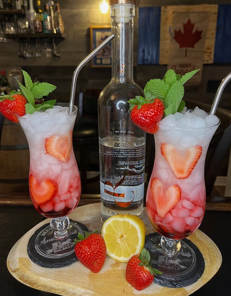 Love Punch cocktail from Lagos, Nigeria — a refreshing layered strawberry and coconut vodka drink with crushed ice, strawberry hearts, and mint garnish. Canada Day special.