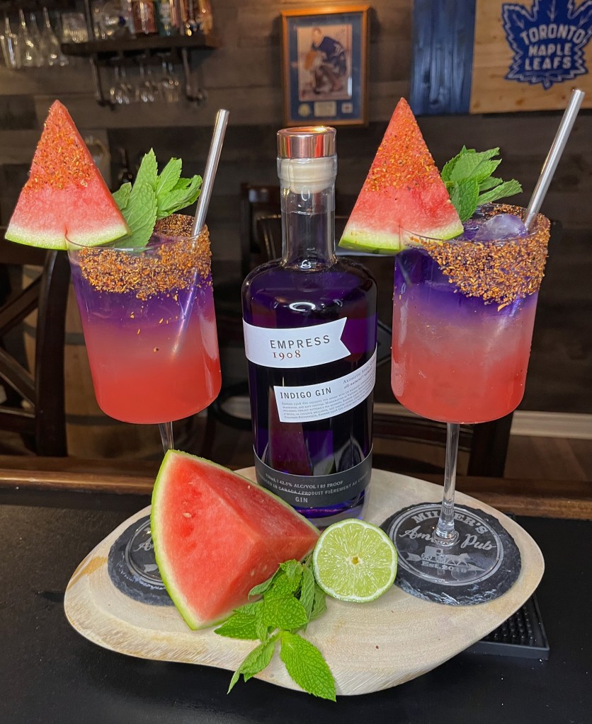 Low-calorie Watermelon Mint Gin Fizz in a stemmed glass with Tajin rim, muddled watermelon and mint, club soda, and a vibrant Empress Gin float, garnished with a Tajin-dusted watermelon wedge and fresh mint sprig.