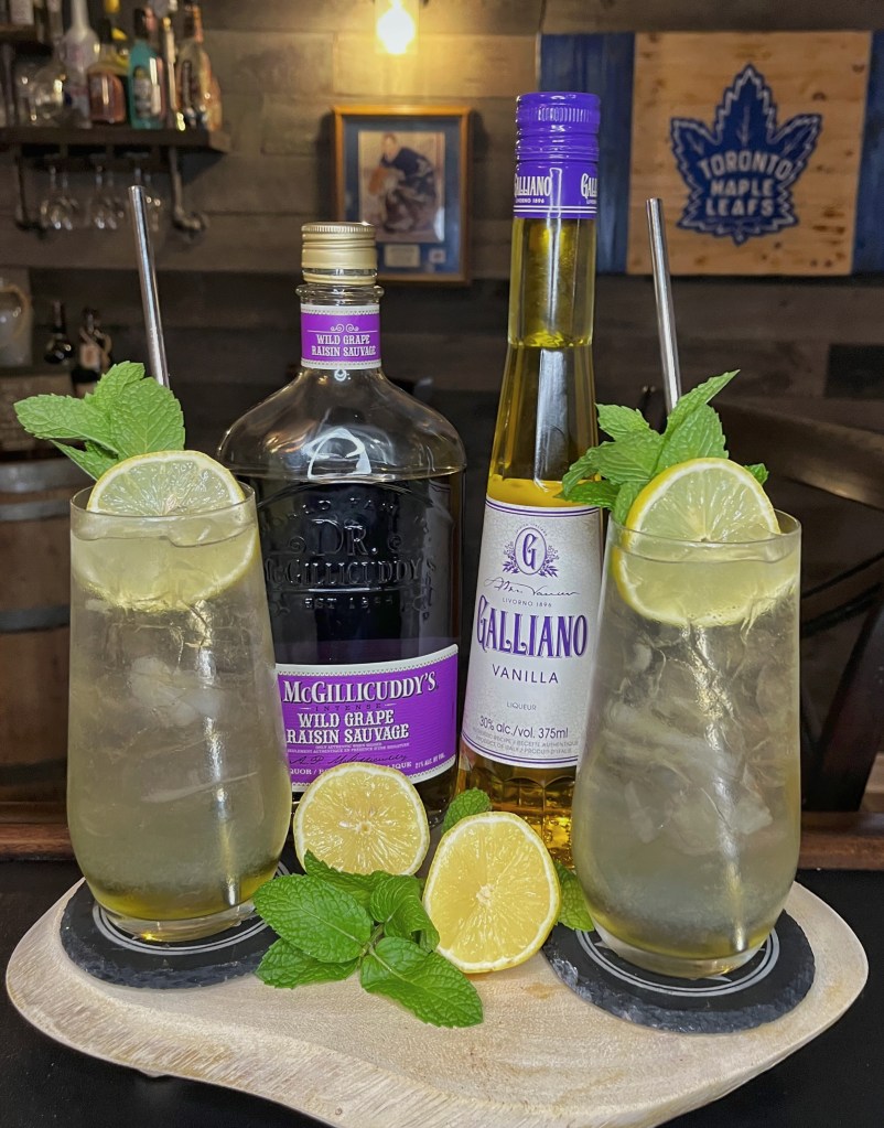 Grape Icecream cocktail in tall glasses with fresh lemon and mint, served beside McGillicuddy’s Wild Grape and Galliano Vanilla bottles